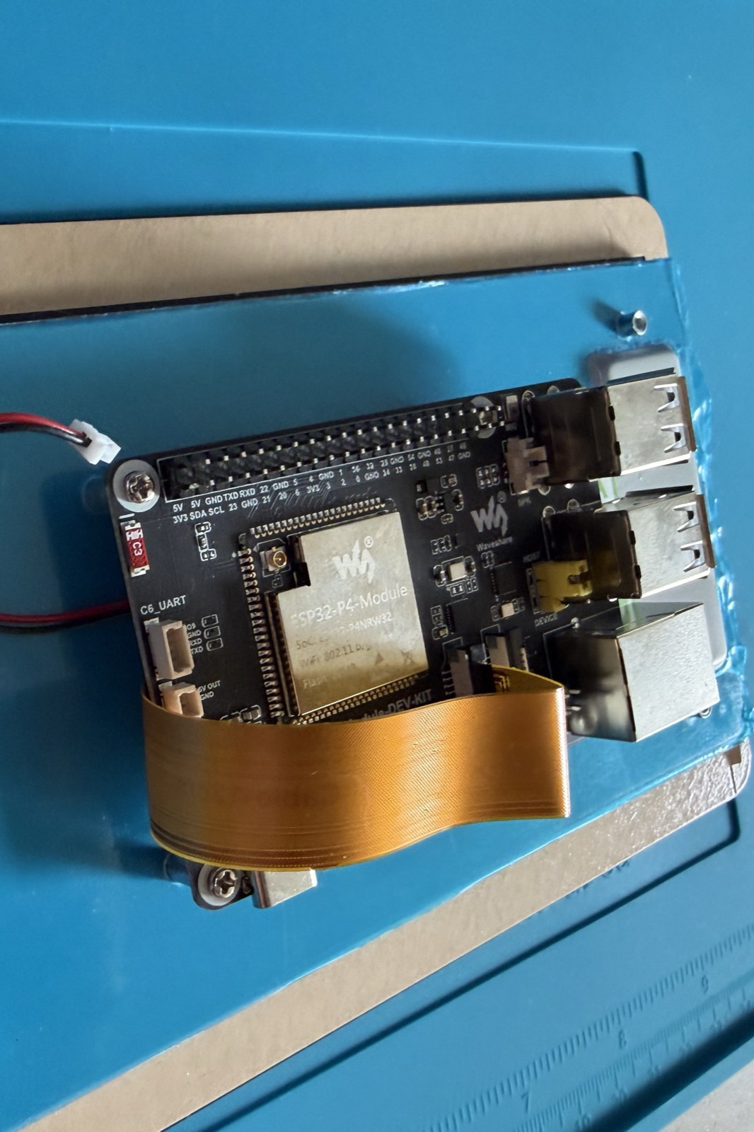 Close view of the ESP32-P4 module, its USB and Ethernet ports, and the ribbon cable curving away to the DSI touchscreen.