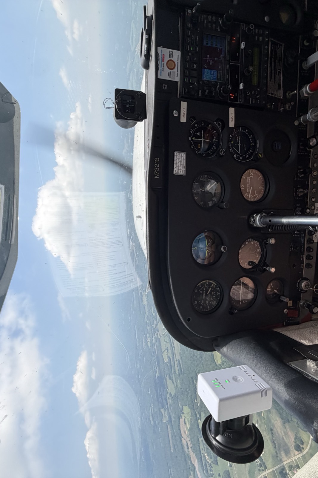 The instrument panel of a Cessna 172 in flight, with farmland and a cumulus cloud visible through the windscreen.